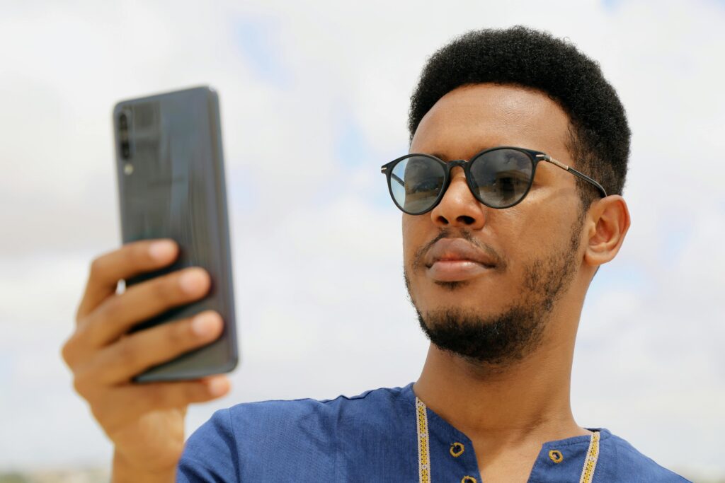 pexels-photo-5558107-5558107 Close-up of an African man wearing sunglasses and using a smartphone outdoors in Mogadishu, Somalia.